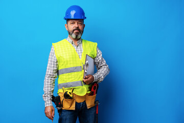 Male builder or handyman in uniform holding clipboard against blue background