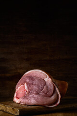 portrait of raw meaty pork knuckle on a cutting board on a dark brown wooden backdrop. artistic moody photo in simple rustic style with copy space