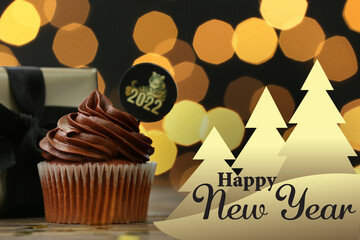 Tasty cupcake for New Year 2022 celebration with gift on table against blurred lights