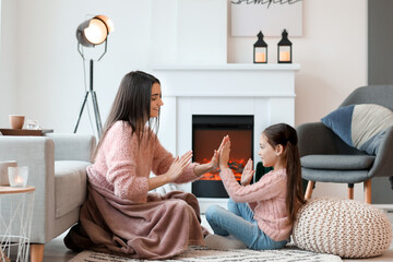 Young mother and daughter resting near fireplace at home