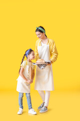 Young mother and daughter with bread and rolling pin on color background