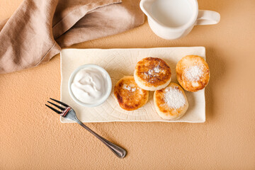 Plate with tasty cottage cheese pancakes and sour cream on color background