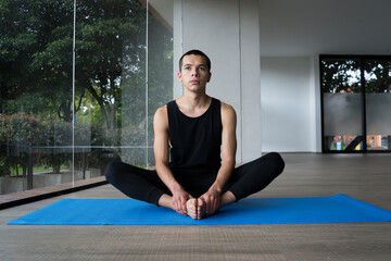 man practicing yoga concept, sitting in baddha konasana exercise in a blue mat