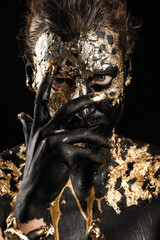 Handsome young man with black and golden paint on body against dark background