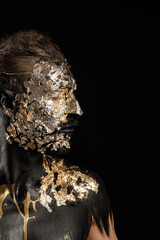 Handsome young man with black and golden paint on body against dark background
