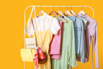 Rack with stylish clothes and bags on color background