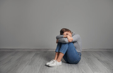 Depressed young woman sitting on floor near grey wall