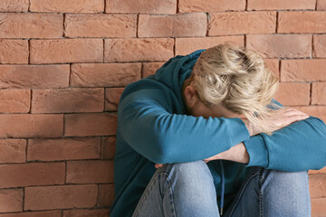 Depressed young man sitting near brick wall