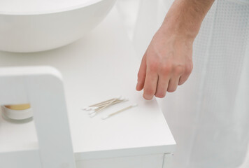 Young man taking cotton bud from table in bathroom, closeup