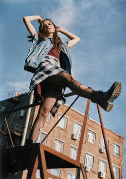 Beautiful grunge (rock) girl takes a step down the stairs. Informal model dressed in jean jacket, checkered shirt, boots and holey tights. Grungy texture effect