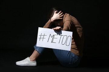 Young woman holding paper with hashtag MeToo on dark background