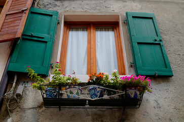 Fototapeta na wymiar a window with green wooden shutters and flowers in flower pots underneath the window in the Italian town of Malcesine