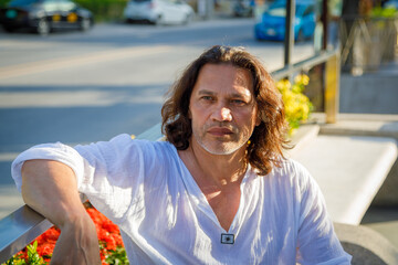 An adult man with long hair and a white shirt looks into the distance.