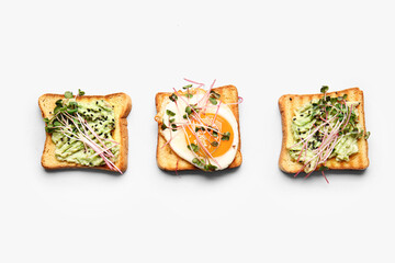 Tasty toasts with avocado, fried egg and micro green on white background