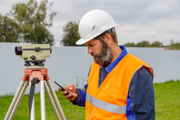 A civil engineer with an optical level looks into a mobile phone.