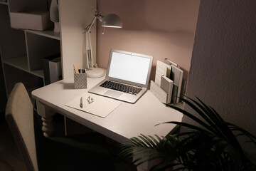 Modern workplace with laptop and glowing lamp near light wall