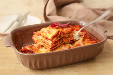 Delicious lasagna with tomato sauce in baking dish on table