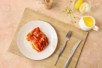 Delicious lasagna with tomato sauce in plate and cutlery on wooden board