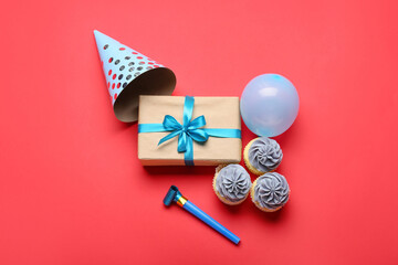 Composition with gift box, party cone, cupcakes and noisemaker on color background