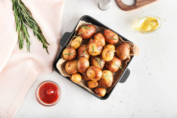 Frying pan with baked potatoes and rosemary on light background