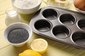 Baking tin and ingredients for delicious muffins with poppy seeds on color wooden table