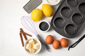 Baking tin and ingredients for delicious muffins with poppy seeds on white wooden table