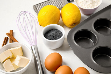 Baking tin and ingredients for delicious muffins with poppy seeds on white wooden table