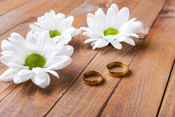 Fototapeta na wymiar Wedding rings and chamomile flowers on wooden table
