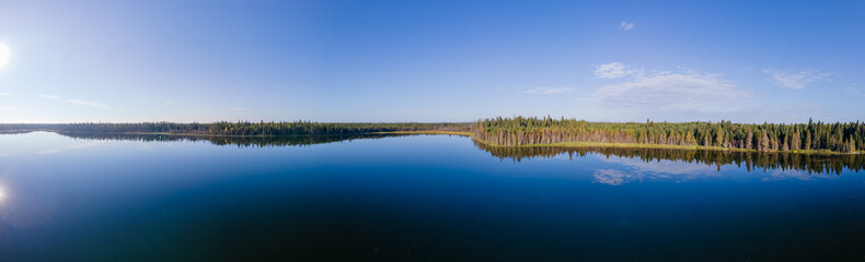 Fototapeta na wymiar Aerial panorama of a large blue colored lake with a shoreline of evergreen trees and reflections of a few scattered clouds. 