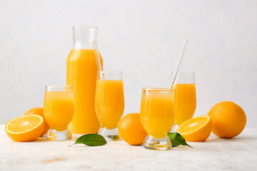 Jug and glasses of tasty orange juice on light background