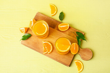 Board with glasses of tasty orange juice on color background