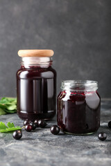 Jars with black currant jam on grey background