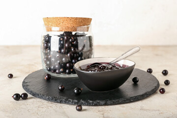 Jar and bowl with black currant jam on light background