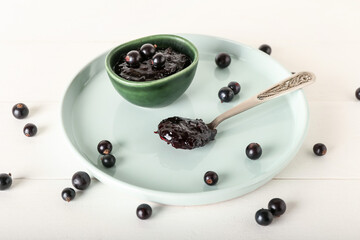 Bowl and spoon with black currant jam on light wooden background