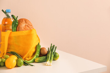Shopping bag with food and drink on table near color wall
