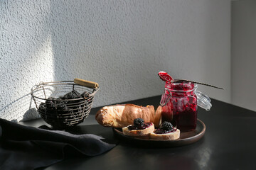 Composition with jar of tasty blackberry jam and sandwiches on table