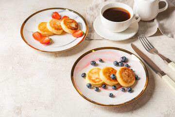Plates with cottage cheese pancakes and berries on light background