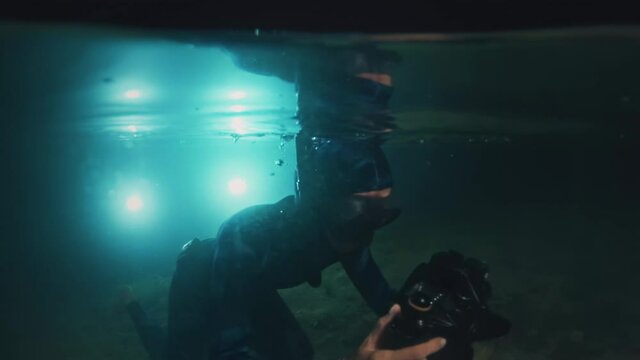 Underwater photographer in night lake. Young woman in wetsuit dives with underwater camera and takes pictures in the lake at night