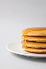 Plate of tasty pancakes with honey on light background, closeup