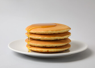 Plate of tasty pancakes with honey on light background
