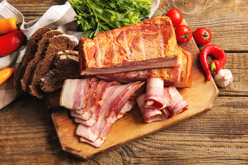 Board with tasty smoked bacon, fresh vegetables and bread on wooden background
