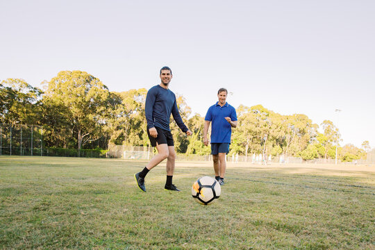 horizontal shot of two men playing soccer in a grass field with trees on a sunny day with clear sky
