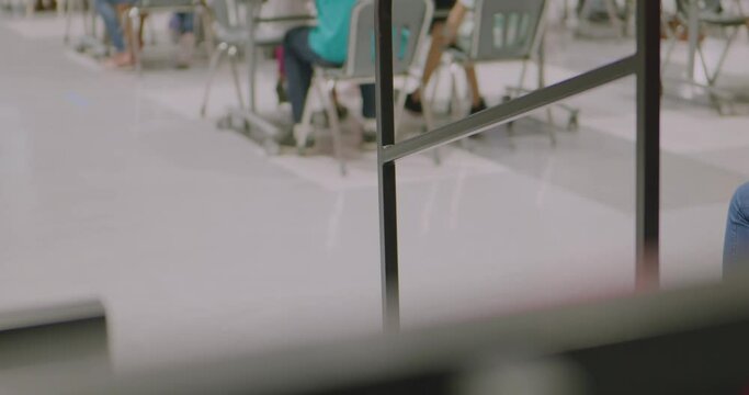 Kids children students sitting in school auditorium cafeteria with kid kicking or swinging legs and feet as focus is on rail with people in the bokeh. In Cinema 4k (4096x2160) 30fps slowed from 60fps.