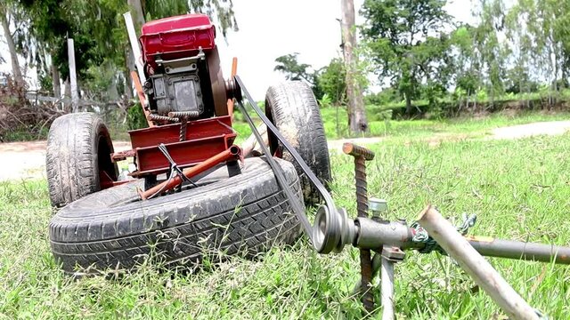 The belt with the pulley is rotating. An old agricultural small engine sent traction by belt to a water pump in the outdoor green rice fields. Selective focus
