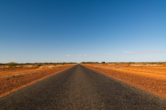 Low, wide view of bitumen road in desert country, converging at  horizon with clear blue sky