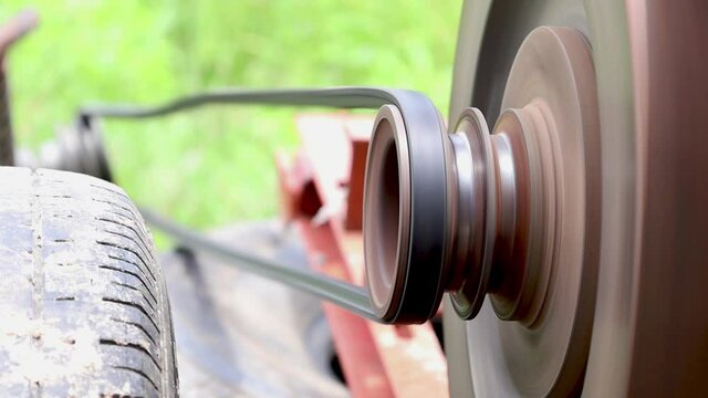 The belt and pulley are spinning. A small old agricultural engine is delivering traction to a water pump in an outdoor rice field. Selective focus