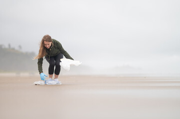 A volunteer collects empty plastic bottles and other garbage on the ocean shore. Environmental...