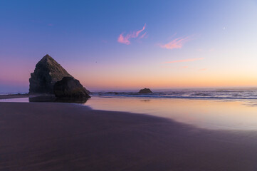 Fototapeta premium Beautiful landscape. Ocean. There are two rocks on the sandy shore. Evening. Sunset. There are light white clouds in the blue sky. Majestic nature. Calm scenes. There is no one in the photo.