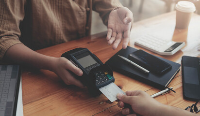 Close-up of asian entrepreneur using EDC to receive credit card for payment from customer in her store.