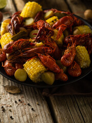 Pieces of corn, boiled crayfish and vegetables on a large platter. Beautiful composition. Close-up. High angle view. Wooden texture. Restaurant, hotel, cafe, cookbook, food design.
